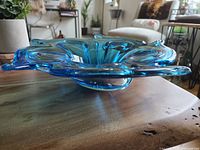 Side view of the vibrant ocean blue art glass dish showing its fluid wavy design, smooth glossy surface, and raised edge.