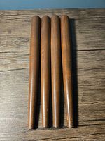 Top-down view of the four solid walnut tapered furniture legs laid side by side, showing their smooth cylindrical shape and finish.