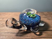 Side view of glass turtle paperweight showing clear glass head, legs, and textured blue shell with green details.