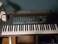 Full view of Yamaha PSR-150 keyboard with power cord resting beside it, showing keys labeled with stickers for learning.