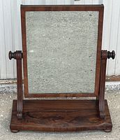 Front view of antique walnut vanity mirror showing pitted mirror and decorative wooden base with side supports.