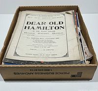 Over 100 sheets of sheet music in a cardboard box, showing aged paper and some wear at edges.