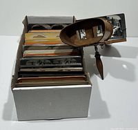 Box containing over 200 stereoview cards and wooden stereoscope positioned to the right.