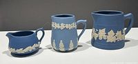 Set of three blue and white Canada art pottery pieces: two pitchers and one creamer, side view showing details and sizes.