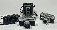 Four vintage cameras displayed together on white background: Black Argus C-Forty-Four with lens, box-style Brownie Reflex, Minolta camera, and Yashica Electro 35.
