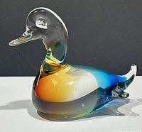 Side angle showing amber, blue, and clear glass with green accents on the neck and tail details.