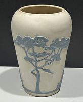 Front view of white ceramic vase with raised blue tree design against dark background.