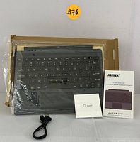 Photo of Arteck HB335 keyboard wrapped in plastic with user manual, small card, and USB charging cable on cardboard box