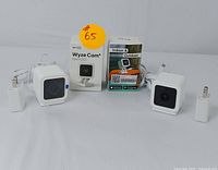 Two white compact Wyze Cam security cameras side by side with their boxes and power adapters on a white backdrop.