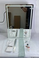 Photo showing mirror face, tempered glass shelf, mounting hardware, packaging and power cord for LED light.