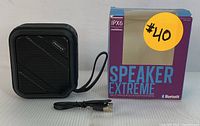 Black Proscan Bluetooth speaker with USB charging cable and original box, showing front and side views with carrying loop attached.