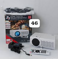 Full set with original box showing a white RCA projector, remote control, power adapter, and a folded screen in storage bag on a white surface.