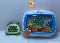 Two toys shown together: Baby Einstein underwater aquarium toy with blue and white plastic frame, and green crab-shaped fidget popper toy.