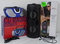 Image showing the Proscan CD Boombox placed on its original box alongside the black Bluetooth speaker with LED lights and its packaging box. Both items have accompanying power cords.