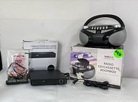 Photo of Sylvania HDMI DVD player, its remote, AV cables, and box next to Proscan CD/cassette boombox with its box, both items arranged on a white surface.