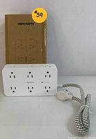 Full view of the power strip with original box behind it. Power strip is white with 12 outlets visible on the front.