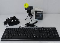 Wired USB keyboard, ergonomic vertical mouse, and webcam with tripod and original box arranged on white surface