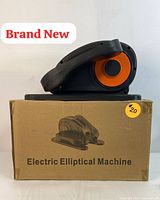 Brand new electric elliptical machine placed on top of its original cardboard box labeled 'Electric Elliptical Machine'. Machine shows black plastic body with orange circular component.