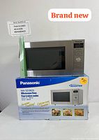 Panasonic NN-SD382S microwave oven on box with brand and model details visible, showing 'brand new' label and size reference.