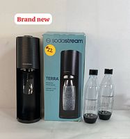 SodaStream Terra sparkling water maker with original box and two reusable bottles shown side by side on white surface.