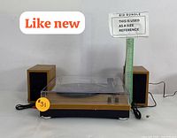 Front view of turntable with dust cover closed, flanked by two wooden speakers and measuring stick.