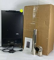 Front view of the black tankless gas water heater showing the 18L marking, digital display, control buttons, power cord, vent pipe components, installation manual, and original cardboard box.