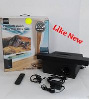 Photo of the subwoofer, remote, auxiliary wired earphones, power adapter, and original packaging showing sound bar system details and branding.