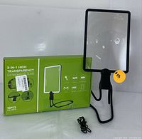 Magnifying glass standing upright next to original green box packaging and USB charging cable.