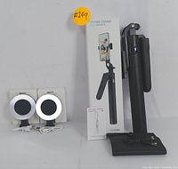 Folded intelligent tracking tripod stand with box and Bluetooth remote control, placed upright with the remote cable visible, alongside two clip-on ring lights with USB cables and packaging.