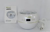 White spherical JJ Autumn digital wax warmer alongside original user manual, showing front LED display and touch buttons, power plugged in.