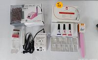 Photo showing assembled nail drill set components: sanding bands, drill bits, drill pen, power box, gel bottles, gel tips box, and nail lamp.