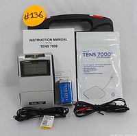 TENS 7000 unit, instruction manual, electrode pads package, 9V battery, and cables arranged in front of carrying case