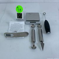 Full view of all items in lot showing digital bow scale with instructions, kitchen scale, ThermoPro thermometer-hygrometer, electric frother, and stainless steel tools including melon ballers and corer.