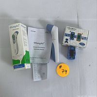 Olangda infrared thermometer shown with original packaging and instruction manual, plus Volueth children's pulse oximeter with original box.