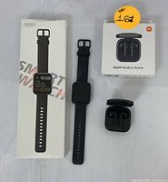 Photo showing smart watch next to its box and Redmi Buds 6 Active earbuds with their box and charging case.