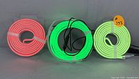Coiled red, green, white neon-style RGB LED strip lights showing colors lit up, with controllers and cables attached