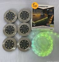 Photo of 8 round stainless steel solar ground lights and coiled Monster multi-color LED light strip with packaging box.