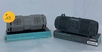 Proscan rugged waterproof speaker and Sylvania IPX6 floating Bluetooth speaker side by side with boxes