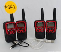 Front view of four Midland X-Talker walkie talkies in red and black, each with LCD screen, buttons, and antenna, shown with two USB charging cables.