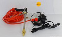 Full view of the water pump connected with long orange hose and metal spray gun with brass nozzle.