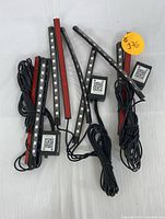 Set of several flexible LED light strips with adhesive backs and smart control modules with QR codes, wires bundled.
