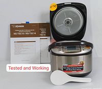 Front view of open rice cooker showing LED display, instruction manuals and spatula laid out.