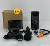 Lot showing the complete backup camera kit including the dashboard screen, backup camera with mounting bracket, portable air compressor with air hose and nozzle, and cables arranged on a white surface with cardboard box in background.