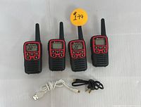 Set of four Midland two-way radios with antennas extended and four charging cables laid out on flat surface