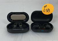 Both pairs of black wireless earbuds in their open charging cases side-by-side, showing earbuds and case interiors.