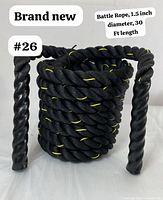 Photo of coiled black braided battle rope with yellow threading, showing the protective grip sleeves on the ends.