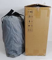 Gray portable carry bag in collapsed form, standing upright against a white background next to cardboard box.