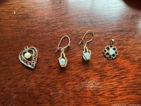 Four pieces displayed on wooden surface: heart pendant, pair of earrings, geometric pendant