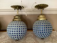 Pair of vintage blue and white hanging lights with spherical globes featuring blue indentations in a golf ball style pattern on a white base, brass mounting hardware on top with scalloped canopy plates, white braided wiring visible.