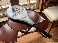Photo of tennis racket in blue and white zipped cloth cover on a wooden table near window.